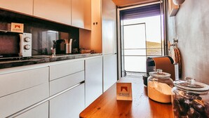 Una cocina moderna con armarios blancos, encimera de madera, una cafetera y frascos de aceitunas.