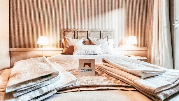 Una habitación de hotel con una cama, dos lámparas de noche, un cabecero de madera y un cartel que dice 'GHT HOUSE'.