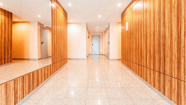 Un pasillo moderno con paneles de madera y suelo pulido, que conduce a una puerta al final.