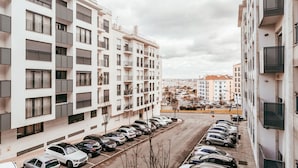 Un edificio residencial de varios pisos con balcones, un estacionamiento y vistas a un paisaje urbano distante.