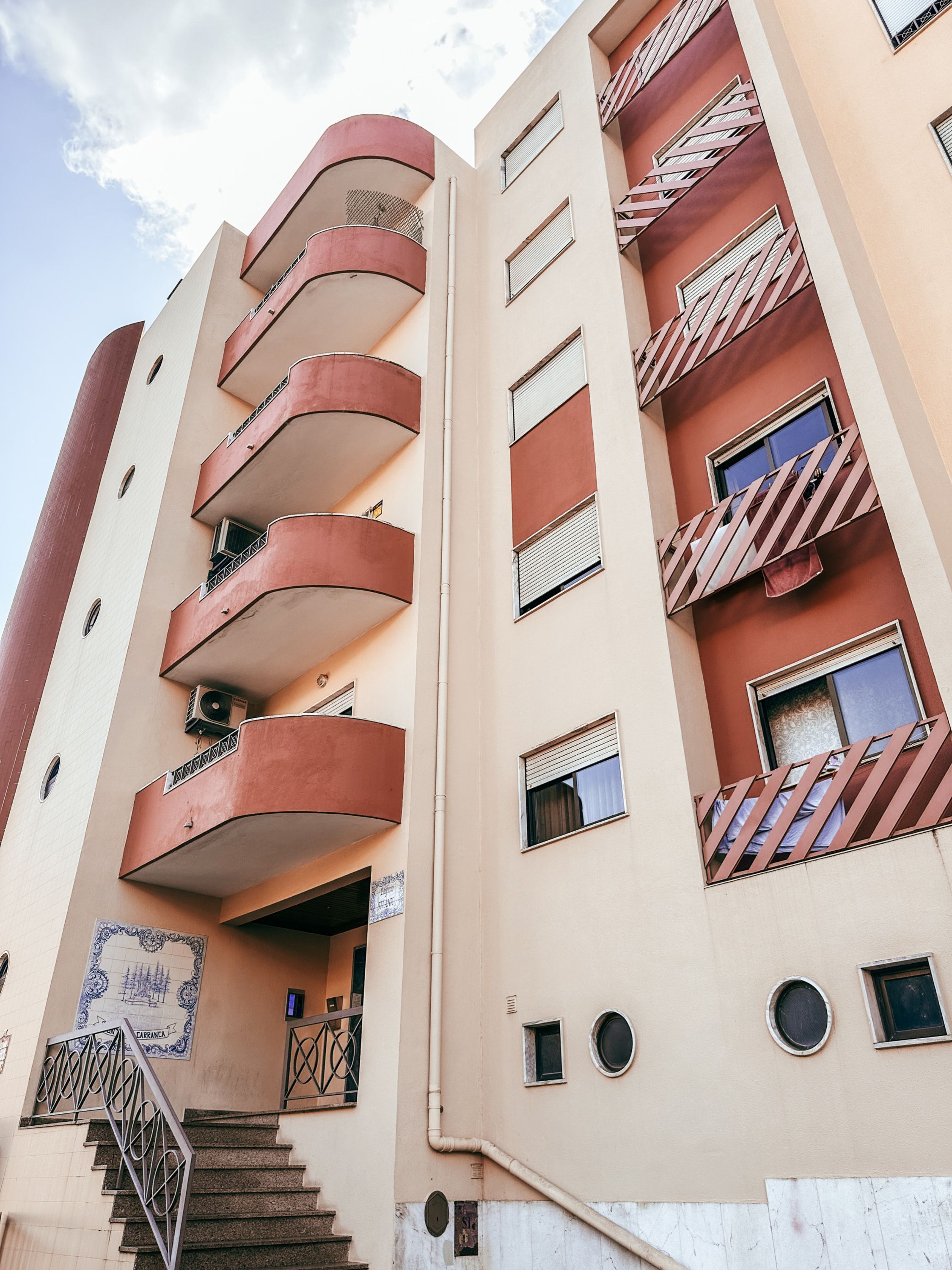 A multi-story building with balconies, a staircase, and a mural.
