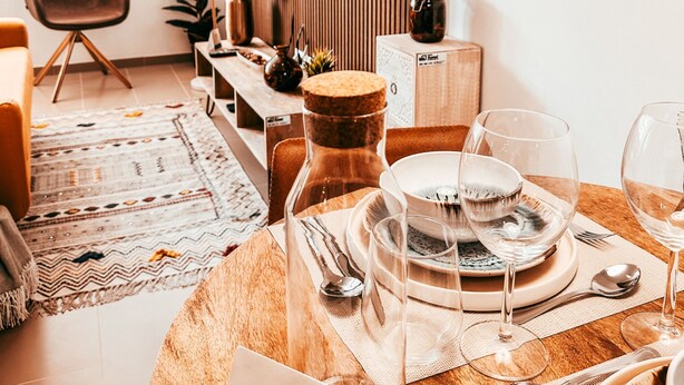 Una sala de estar moderna con comedor listo para una comida, un televisor montado en una pared de paneles de madera y una ventana con persianas.