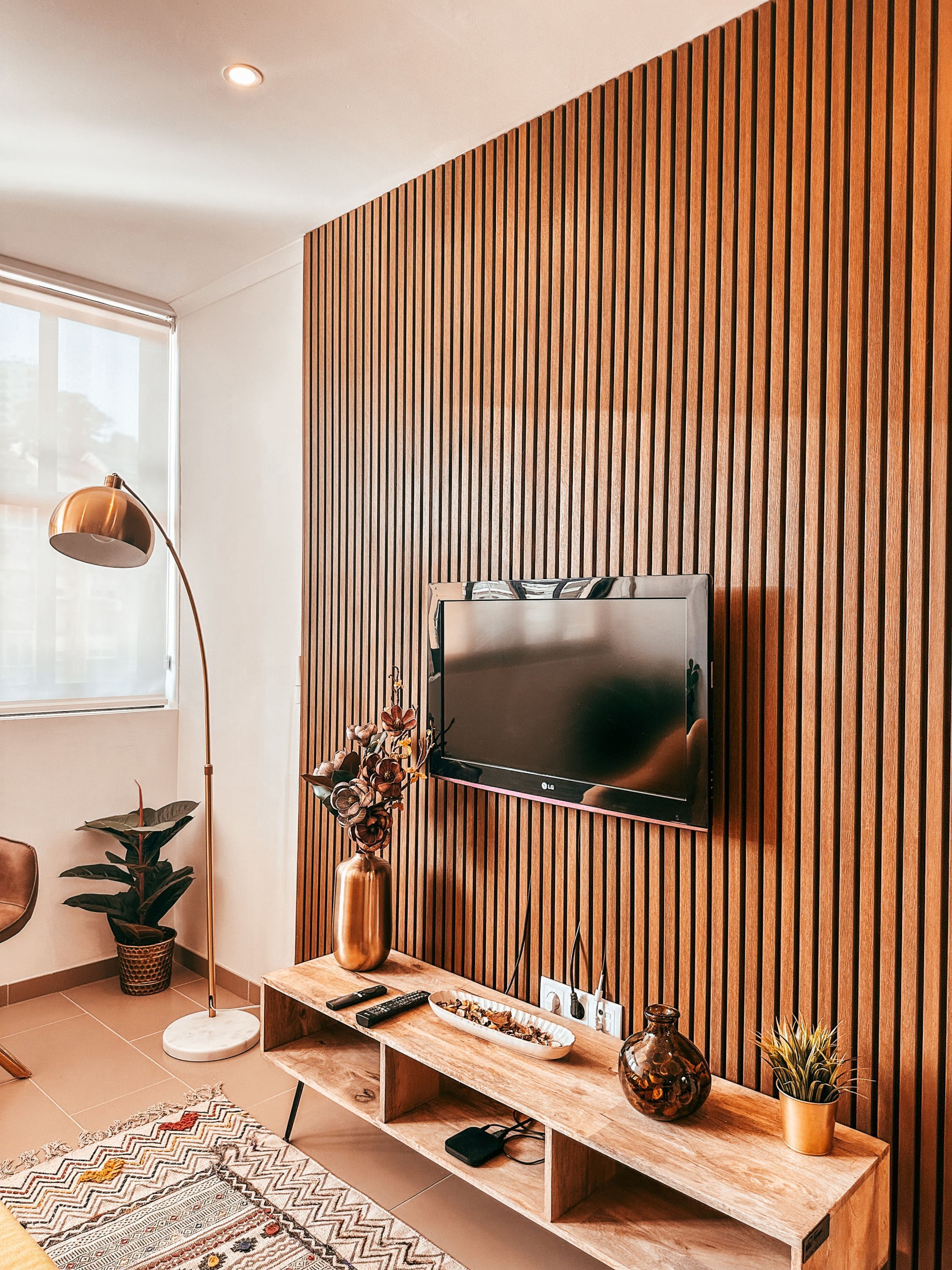 A modern living room with a mounted TV, wooden panel wall, a console table with decorative items, and a floor lamp.