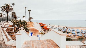 A beachside hotel with a staircase leading to the beach, outdoor seating, and umbrellas. - Beach House By Gt House (Silves)