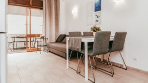 A dining area with a table and chairs, a sofa, a window with curtains, and wall-mounted artwork. - Beach House By Gt House (Silves)