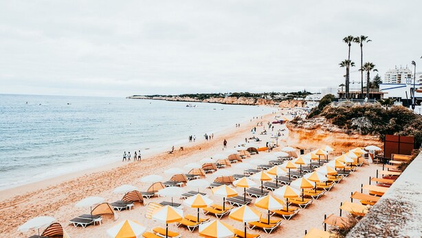 A beach with rows of sun loungers and umbrellas, a sandy shore, and a calm sea. - Beach House By Gt House (Silves)
