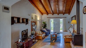 A spacious living room with wooden beams, a fireplace, a television, and a bookshelf. - Jacarand Apartment in Quinta Velha by GT House (Portimão)