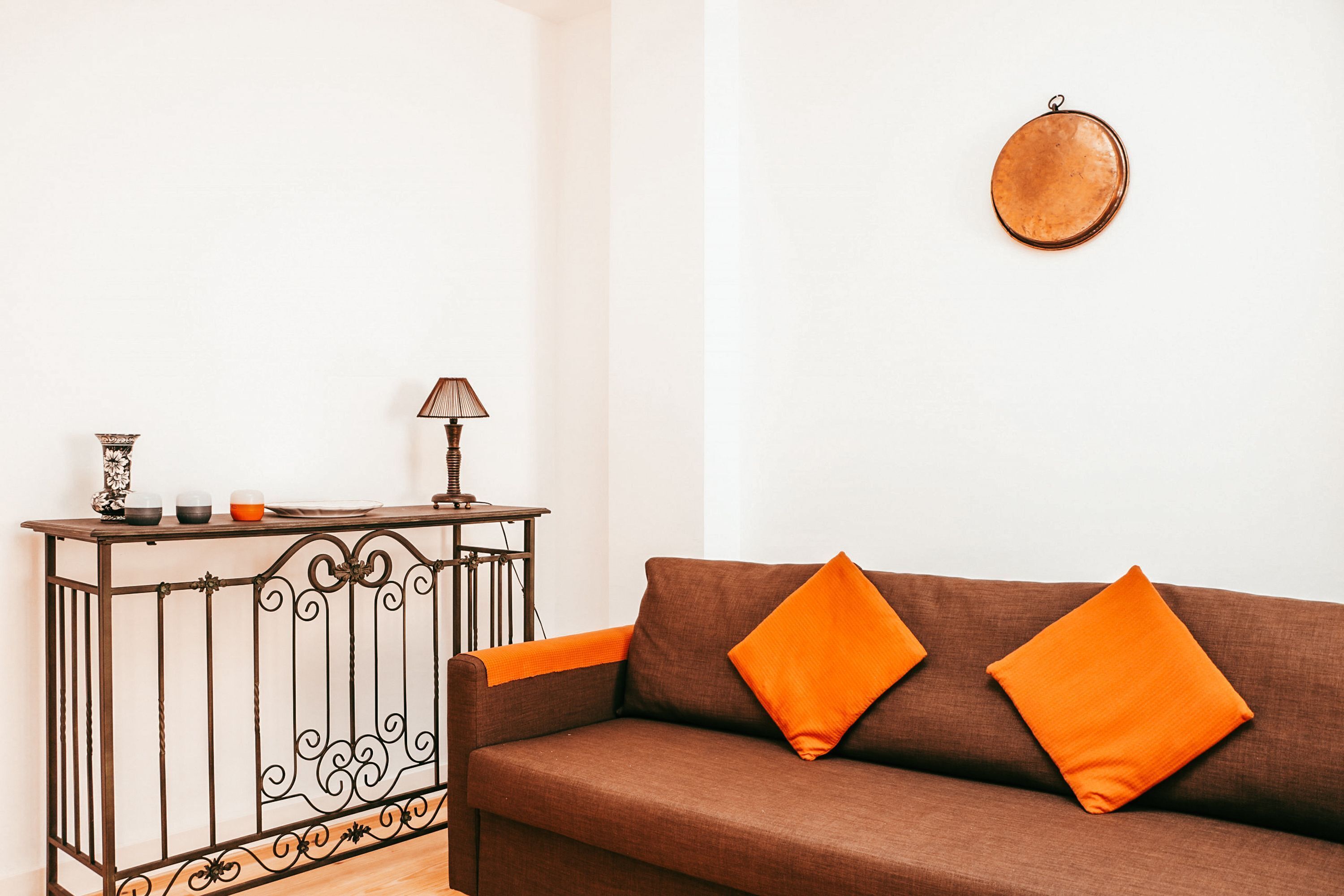 Un canapé marron avec des coussins orange, une console en métal surmontée d’une lampe, et un élément de décoration circulaire fixé au mur.