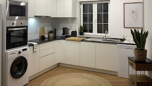 A modern kitchen with built-in appliances, a dining area with a chair, and a potted plant. - Goleg Boutique Apartment By Gt House (Golega)