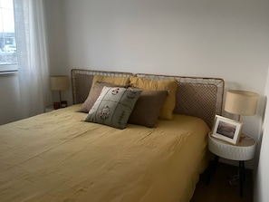 Een bed met hoofdeinde, kussens, een nachtkastje met lamp en een fotolijst.