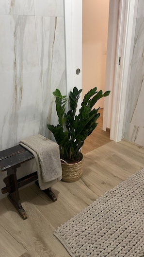 Een kamer met een marmeren wand, een bank met een plaid, een plant in pot en een geweven vloerkleed.