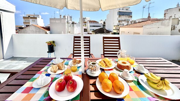 Eine Dachterrasse mit einem Tisch, der für ein Frühstück gedeckt ist, mit Früchten, Gebäck und Getränken.