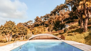 A swimming pool with a covered bridge, surrounded by trees and a hilly landscape. - Oliveira s Houses By Gthouse (Sintra)