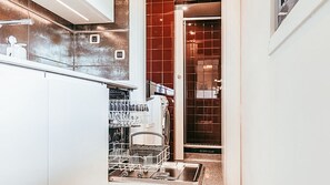 A narrow kitchen with a dishwasher, a washing machine, and a small window. - Trendy Apartment River View By Gthouse (Lisbon)