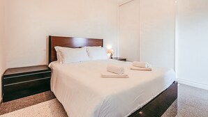 A neatly made bed with white linens, a wooden headboard, and two rolled towels on the bed. - Trendy Apartment River View By Gthouse (Lisbon)