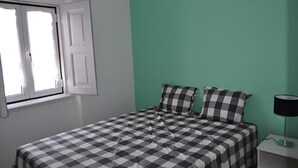 Une chambre avec une couvre-lit à carreaux, une fenêtre avec des volets blancs et un mur vert.