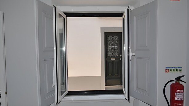 Un couloir avec une porte donnant sur une pièce, un extincteur fixé au mur et une porte ornée d’un motif décoratif.