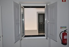 Een gang met een deur die naar een kamer leidt, een brandblusser bevestigd aan de muur, en een deur met een decoratief patroon.