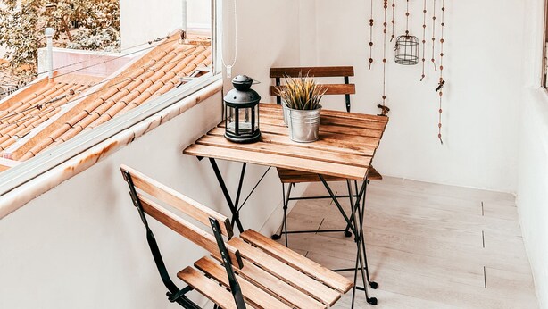 Un balcón con una mesa de madera, dos sillas, un farol y un adorno colgante.