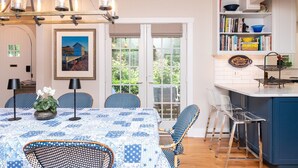 Un coin repas avec une table dressée pour quatre personnes, un lustre et une vue sur le jardin, visible à travers la porte vitrée.