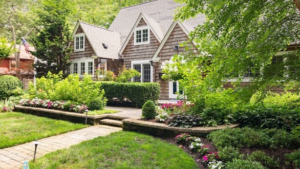 Une maison à deux étages avec un jardin bien entretenu, un chemin pavé et un petit étang.