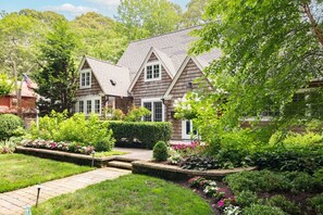 A two-story house with a well-maintained garden, a paved pathway, and a small pond. - Quiet Pines Escape | Private Pool | BBQ | Beach (Rehoboth Beach)