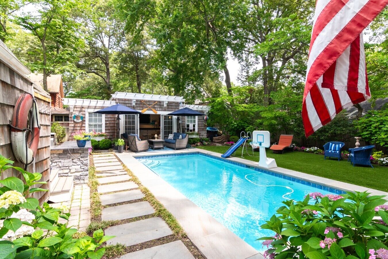 Ein Garten mit Schwimmbad, überdachter Terrasse und einer Flagge.