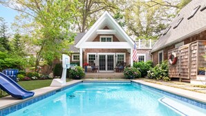 Une piscine avec un toboggan, une maison avec une véranda et un drapeau.