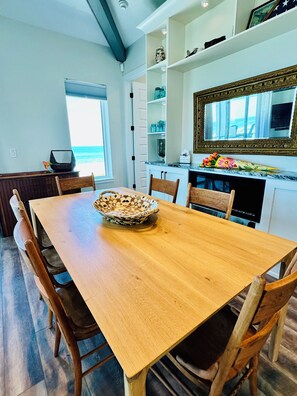 Un coin repas avec une table en bois, des chaises, un vase décoratif et une vue sur l’océan par la fenêtre.
