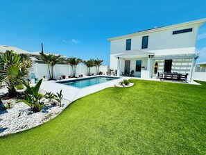 Une maison moderne dotée d’une piscine, d’un patio couvert et d’une pelouse bien entretenue.