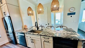 Cocina con encimera de granito, electrodomésticos de acero inoxidable y una isla grande con pileta. Hay tres lámparas colgantes sobre la isla.