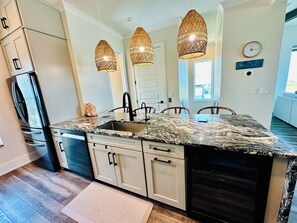 A kitchen with a granite countertop, stainless steel appliances, and a large island with a sink. There are three pendant lights above the island. - Beautiful Oceanfront House with Pool in Flagler Beach (Flagler Beach)