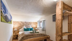 A bedroom with a wooden bed, a wooden headboard, a small bedside table, a lamp, a window with curtains, and a wooden wardrobe. - Chalet Hüttenzauber (Kirchberg in Tirol)