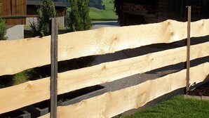 A wooden deck with a view of mountains, a wooden fence, and a building with a sloped roof. - Chalet Hüttenzauber (Kirchberg in Tirol)