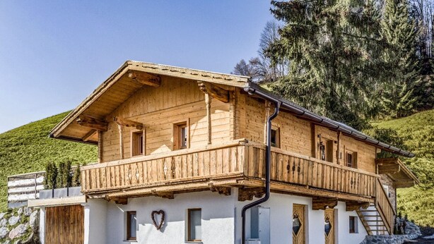 A two-story wooden chalet with a balcony, stone foundation, and a heart-shaped decoration. - Chalet Hüttenzauber (Kirchberg in Tirol)