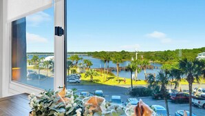 A view from a hotel room window overlooking a parking lot with cars, palm trees, and a body of water. - Beachfront Gem Lakeside Resort Amenities Near 30A (Panama City Beach)