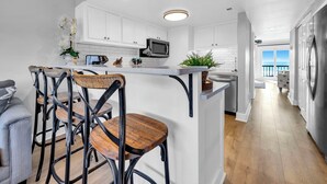 A modern kitchen with white cabinets, a central island, bar stools, and a view to the outside. - Beachfront Gem Lakeside Resort Amenities Near 30A (Panama City Beach)