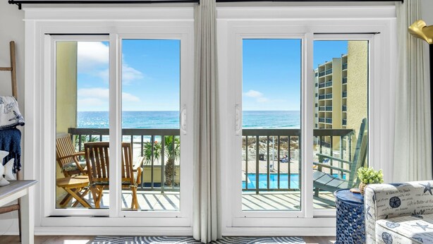 A balcony with a view of the ocean and a pool, wooden chairs, a patterned rug, and a sofa with a nautical theme. - Beachfront Gem Lakeside Resort Amenities Near 30A (Panama City Beach)