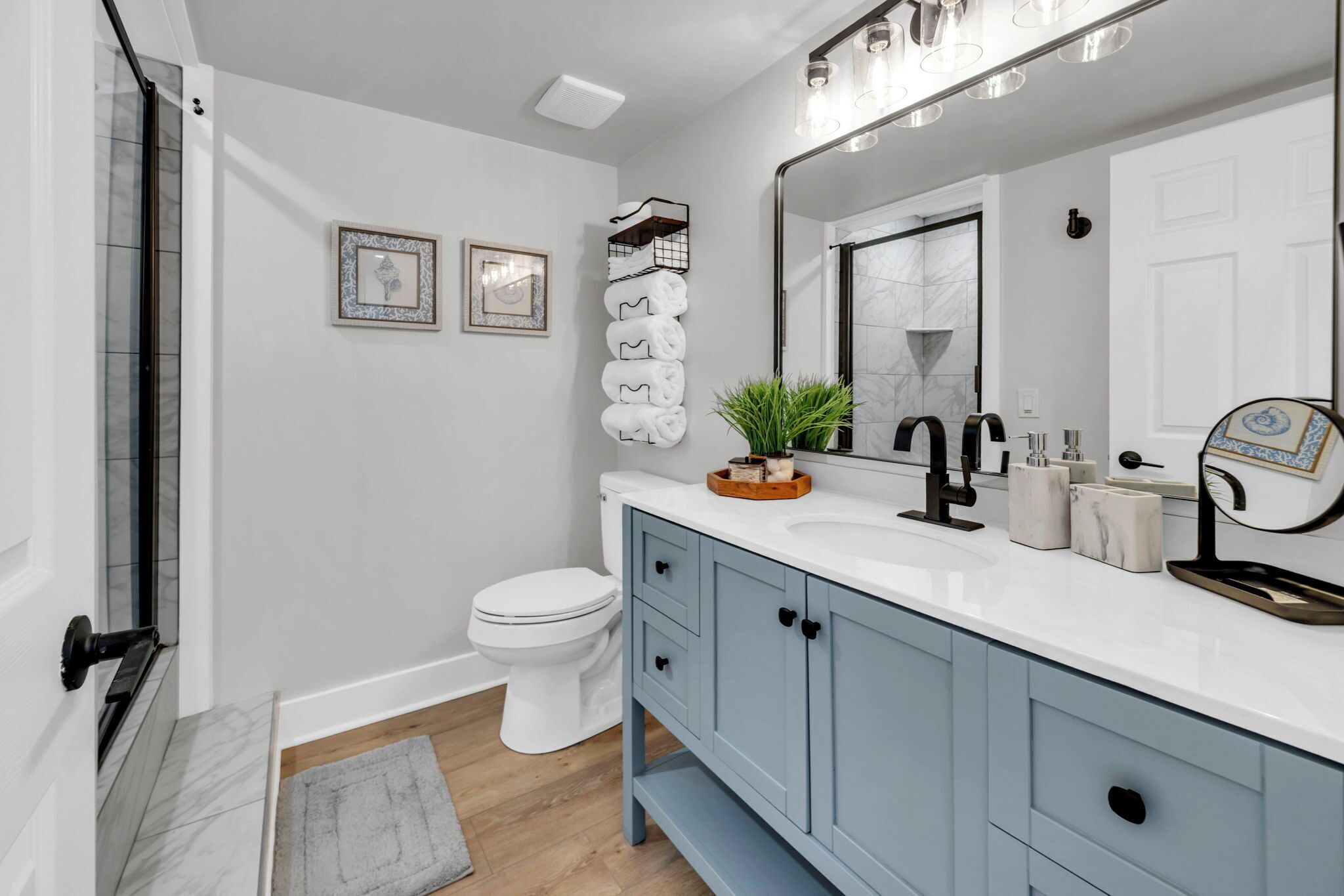 Un baño con inodoro blanco, tocador azul, un espejo grande y zona de ducha.
