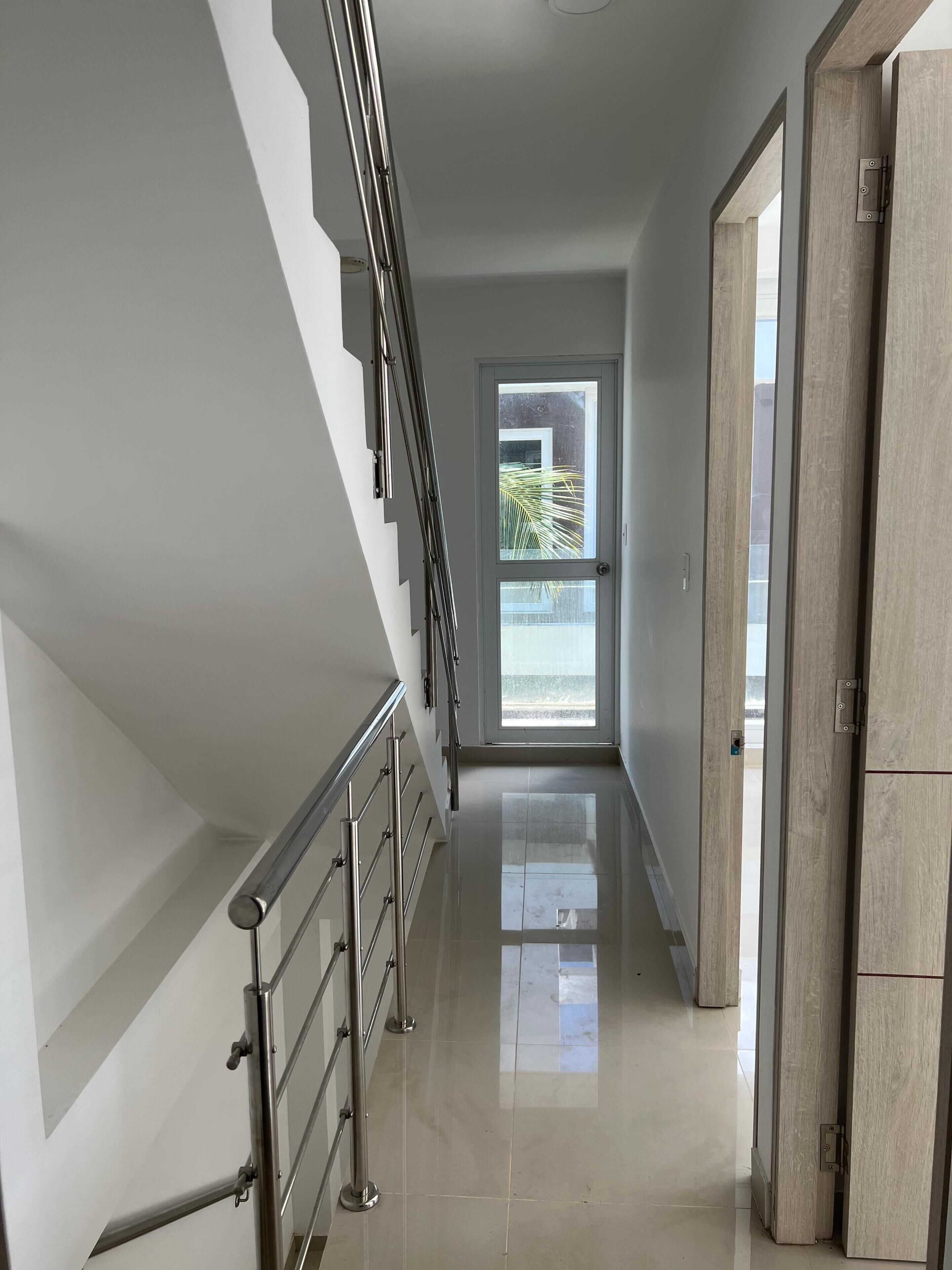 Un couloir avec un escalier, une porte dotée d’une fenêtre et un meuble en bois.