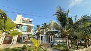 A modern two-story building with a glass facade, palm trees, and a well-maintained lawn. - Charming 3-bedroom condo with AC right by the beach in cozy Coveñas (Coveñas)