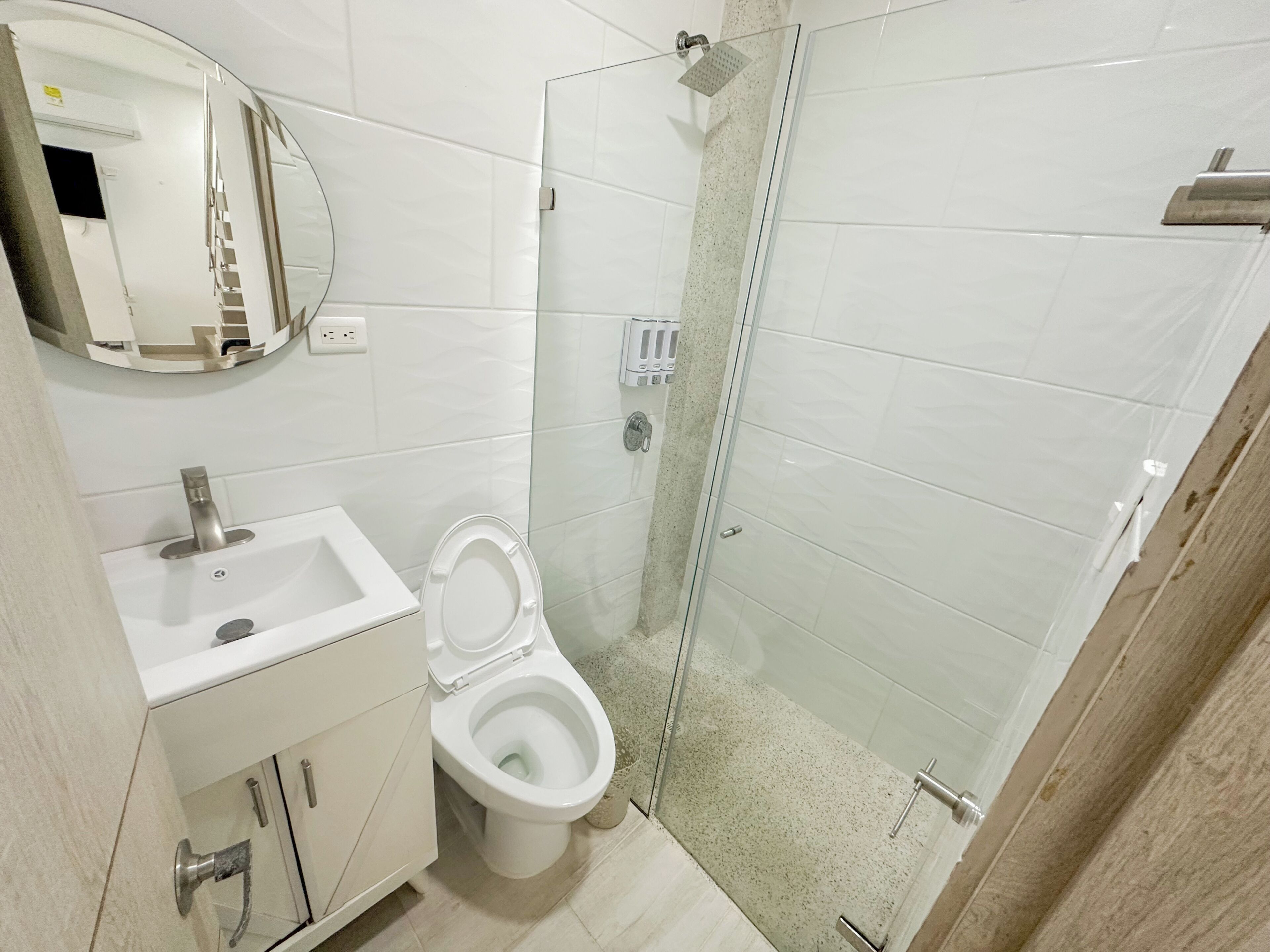 A bathroom with a toilet, sink, mirror, and glass shower enclosure.
