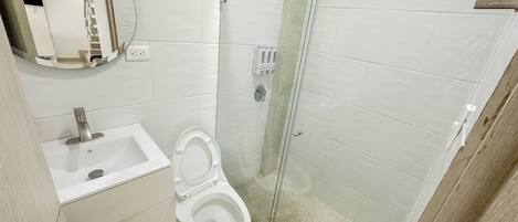 A bathroom with a toilet, sink, mirror, and glass shower enclosure.