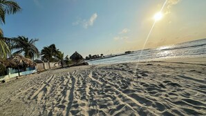 A beach with footprints, palm trees, and a thatched-roof hut. - Charming 3-bedroom condo with AC right by the beach in cozy Coveñas (Coveñas)
