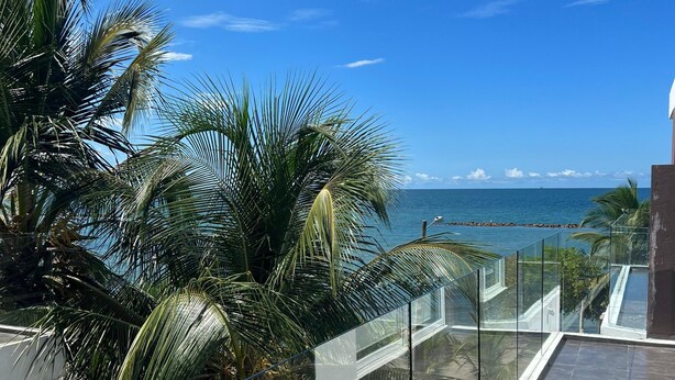 A modern pool area with glass railings, palm trees, and a view of the ocean. - Charming 3-bedroom condo with AC right by the beach in cozy Coveñas (Coveñas)