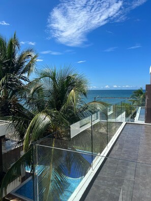 A modern pool area with glass railings, palm trees, and a view of the ocean.