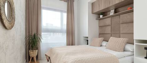 A modern bedroom with a bed, a bedside table, a wall-mounted shelf, a potted plant, and a large mirror.