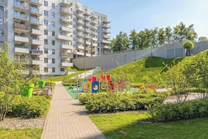 Ein mehrstöckiges Wohngebäude mit Balkonen, einem gepflasterten Weg und einem Spielplatz mit bunten Spielgeräten.