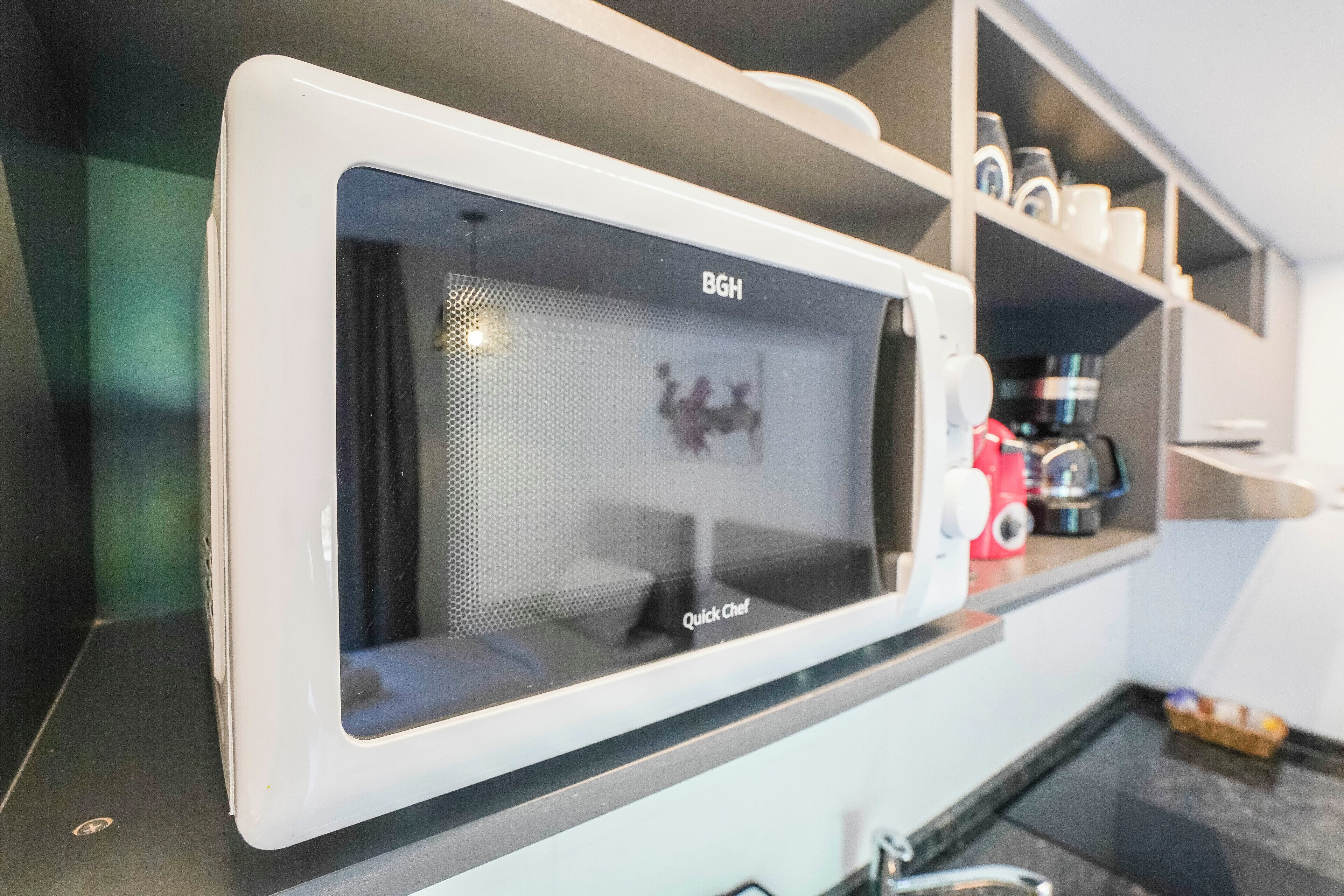 A white microwave oven with a mesh window, a coffee maker, and a toaster on a kitchen counter.