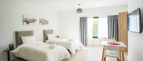 Ein Hotelzimmer mit zwei Betten, einem Schreibtisch, einem Sessel, Bildern an der Wand und einem an der Wand befestigten Fernseher.